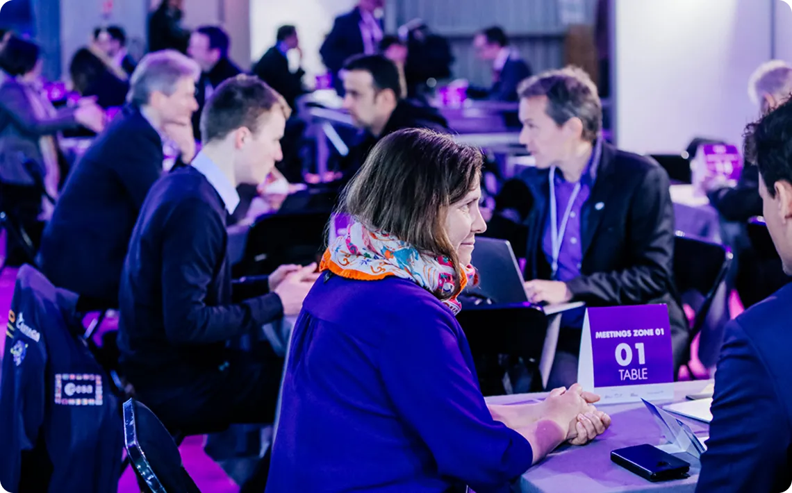 Des professionnels en réunion assis à une table marquée zone rencontres 01 dans une salle animée.