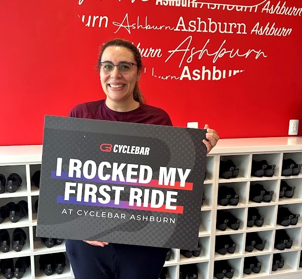 New rider holding an I Rocked My First Ride sign after her first indoor cycling class at CycleBar Ashburn