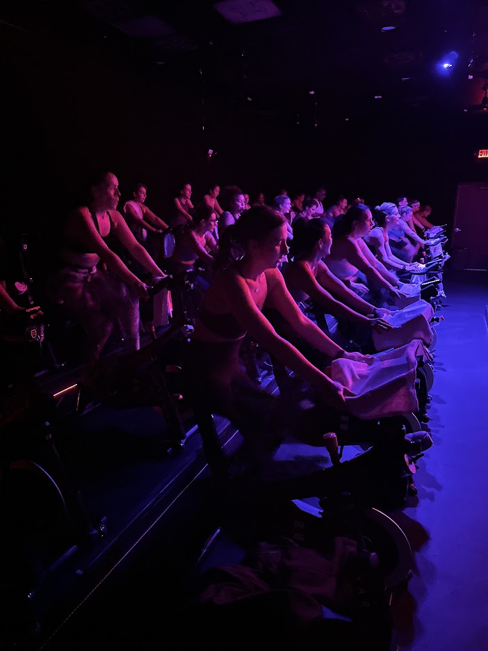 Rows of riders cycling together under purple and blue lights at CycleBar Ashburn.
