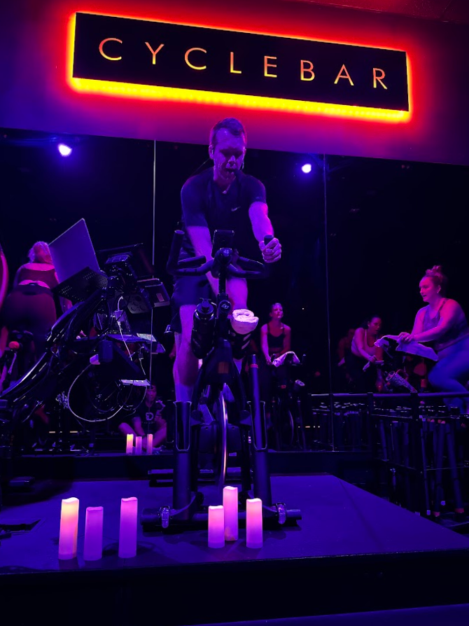 A rider on a bike in the purple-lit CycleBar Ashburn studio, with candles on the platform.