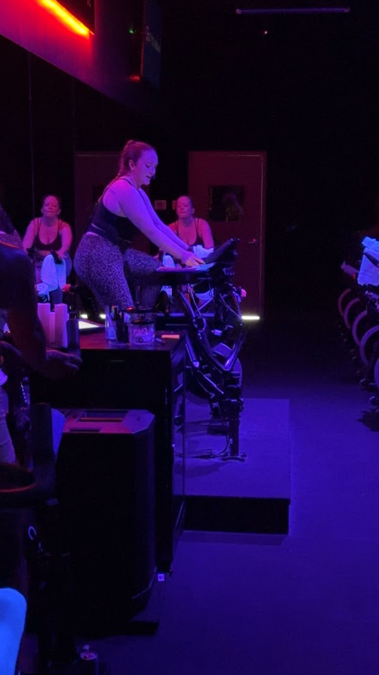 An instructor in a black top and patterned leggings leading a CycleBar Ashburn class from the front bike.
