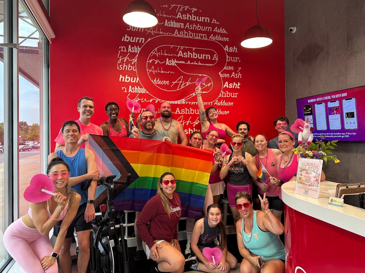 CycleBar Ashburn riders gathered in the studio lobby holding a Pride flag.