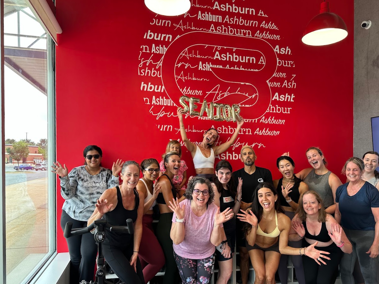 A group celebrating an instructor earning Senior Instructor status in the CycleBar Ashburn lobby.