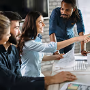 Three colleagues collaborating in an office, with a woman pointing at a computer screen while two men observe.