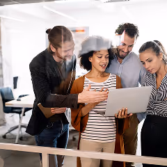 Four diverse colleagues collaborating and looking at a laptop screen in an office setting.