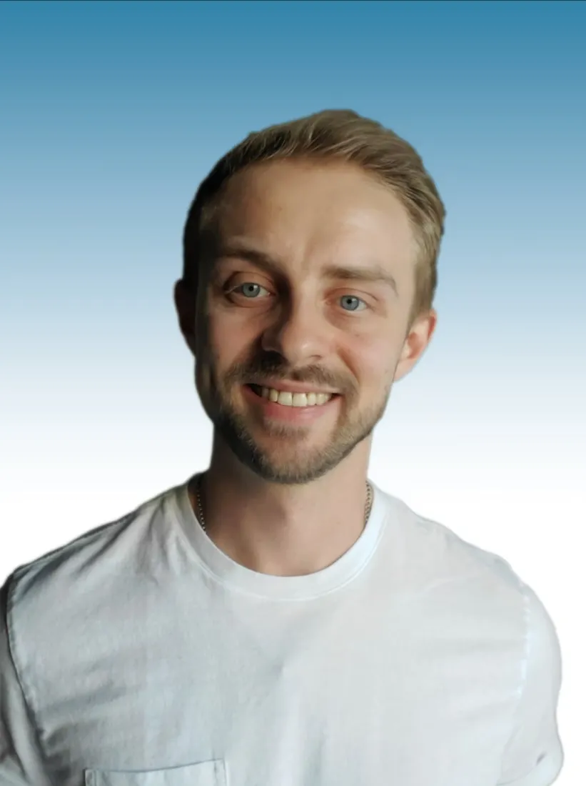 Smiling young man with light brown hair and beard wearing a white t-shirt against a blue gradient background.