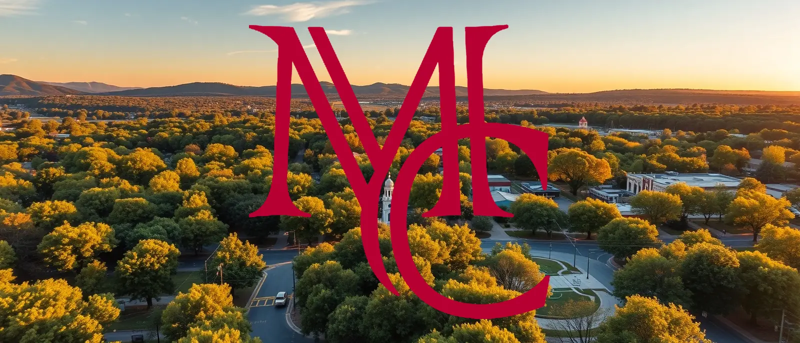 Aerial view of a tree-lined Northwest Arkansas town at golden hour with Ozark hills on the horizon — MCG