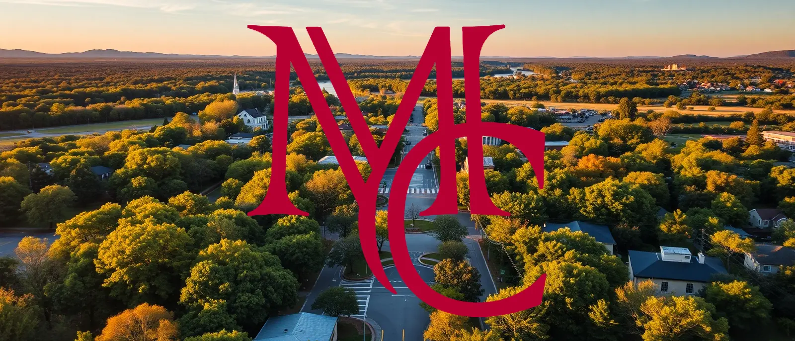 Aerial view of a tree-covered Northwest Arkansas town and its road corridor at sunset — MCG