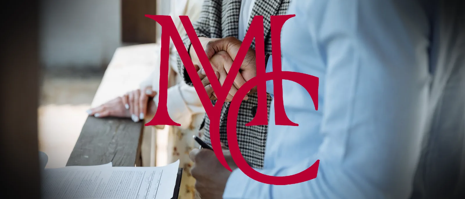 Two people shaking hands over a signed contract at a table — MCG