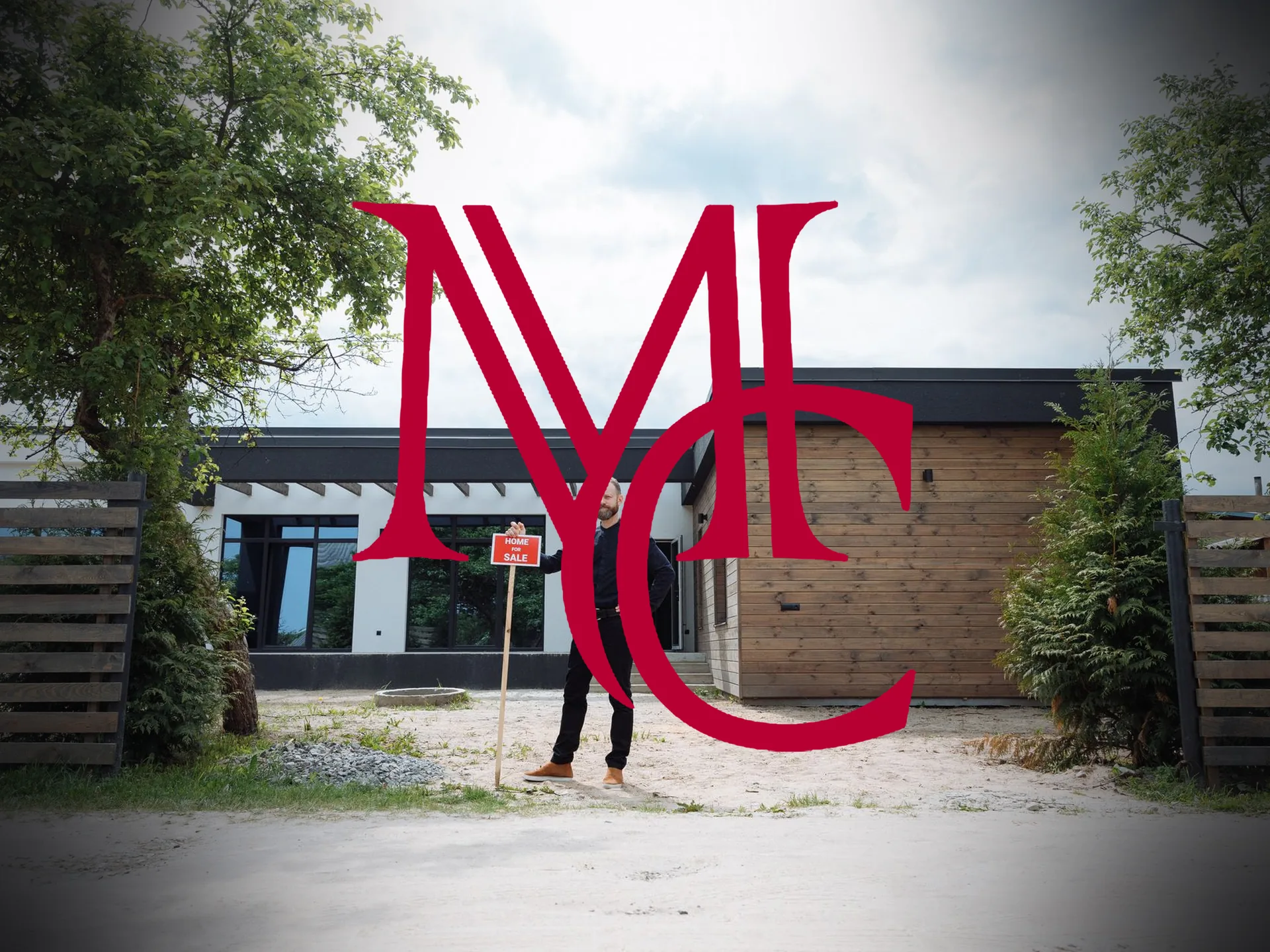 A man standing beside a Home For Sale sign in front of a modern single-story house — MCG
