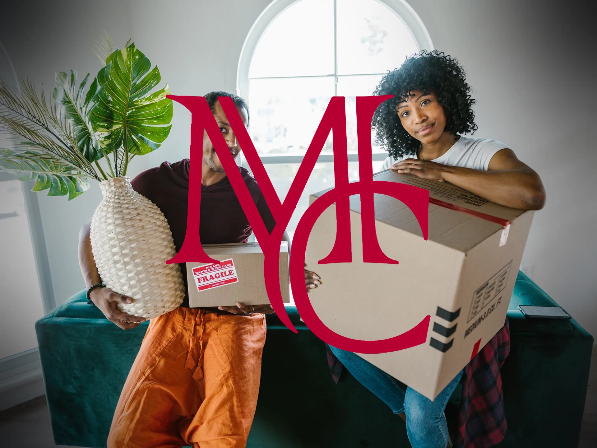 A couple carrying moving boxes and a houseplant into a bright, high-windowed home — MCG