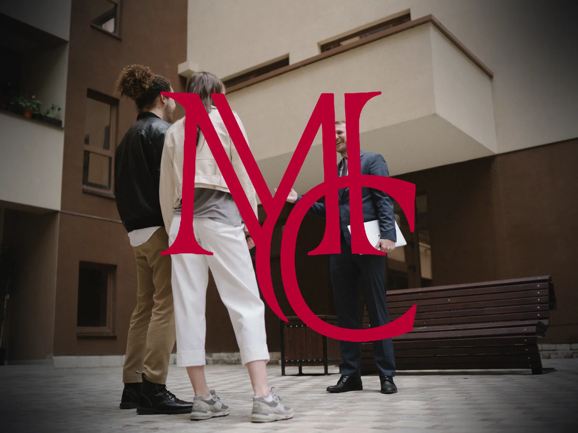 A real estate agent in a suit greeting a couple outside a residential building — MCG