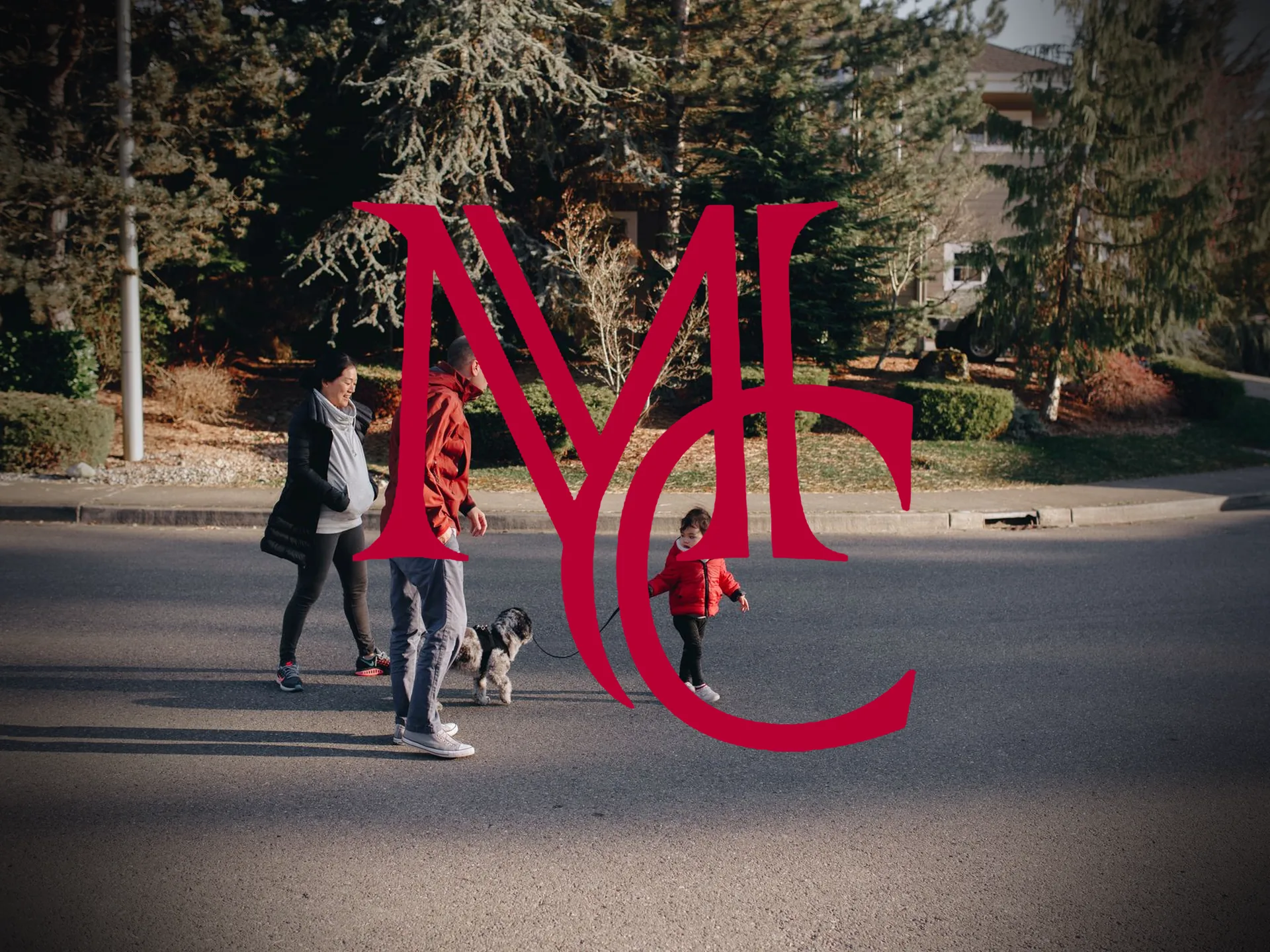 A family walking a dog along a tree-lined residential street in a suburban neighborhood — MCG