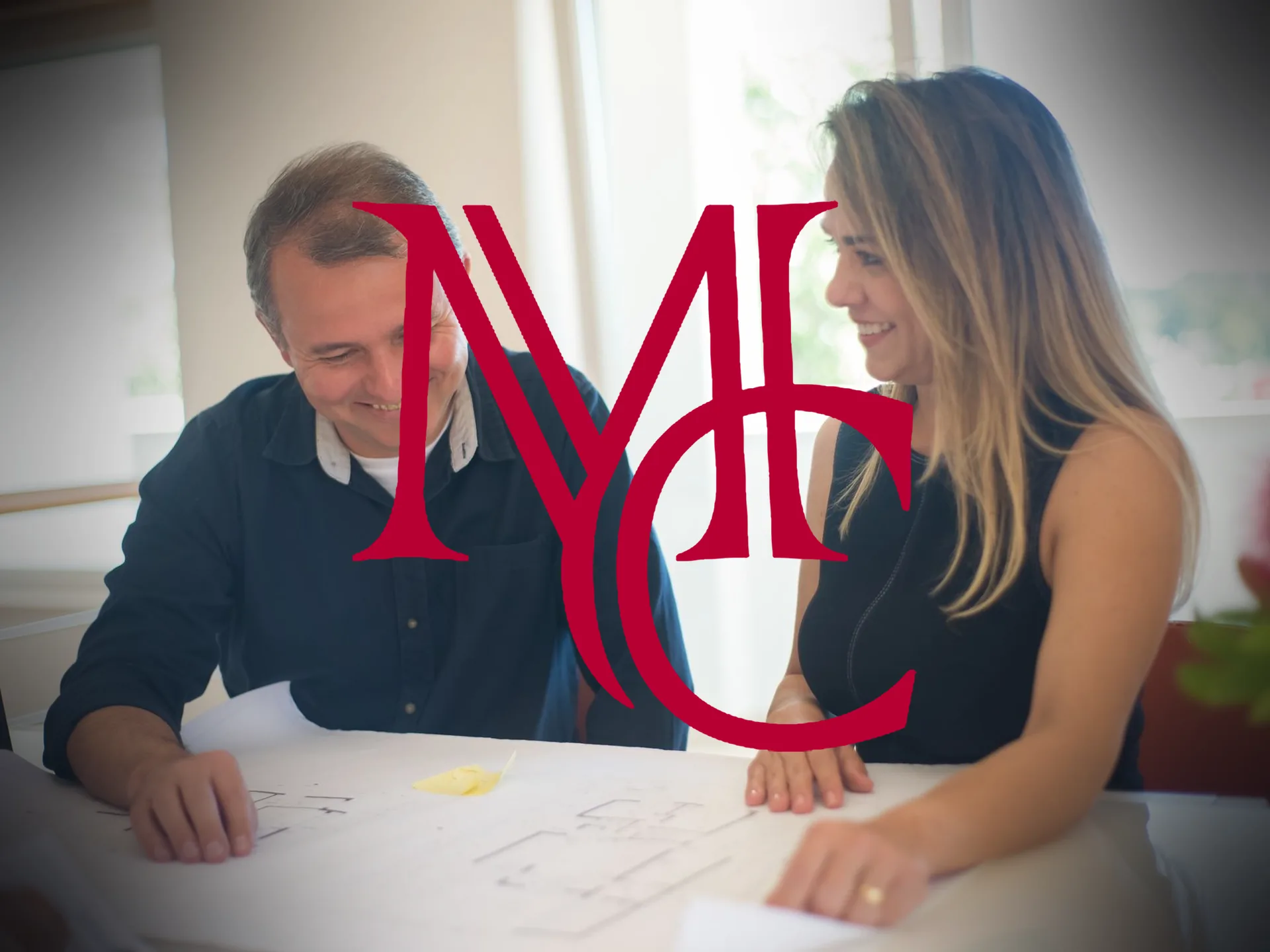 A homeowner and a real estate agent reviewing listing plans together at a sunlit table — MCG
