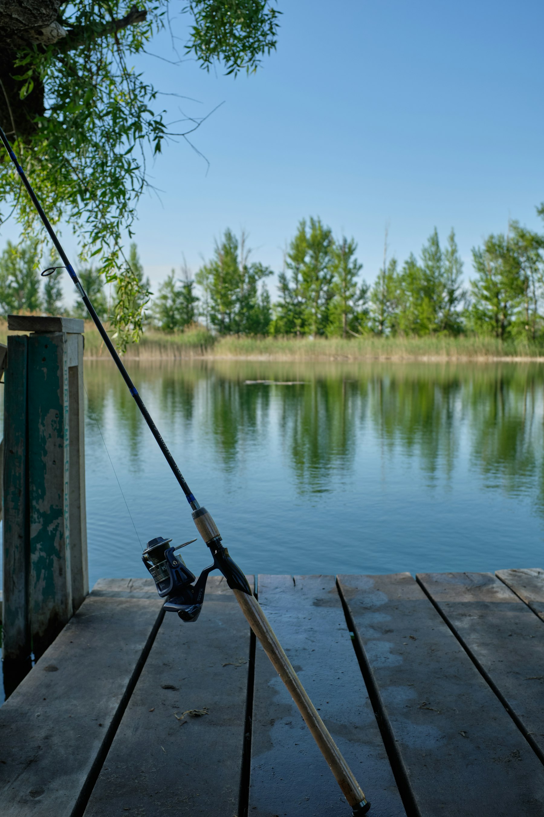 Fishing rod resting on a wooden lake dock at calm water (stock photo, not Lake Bentonville)