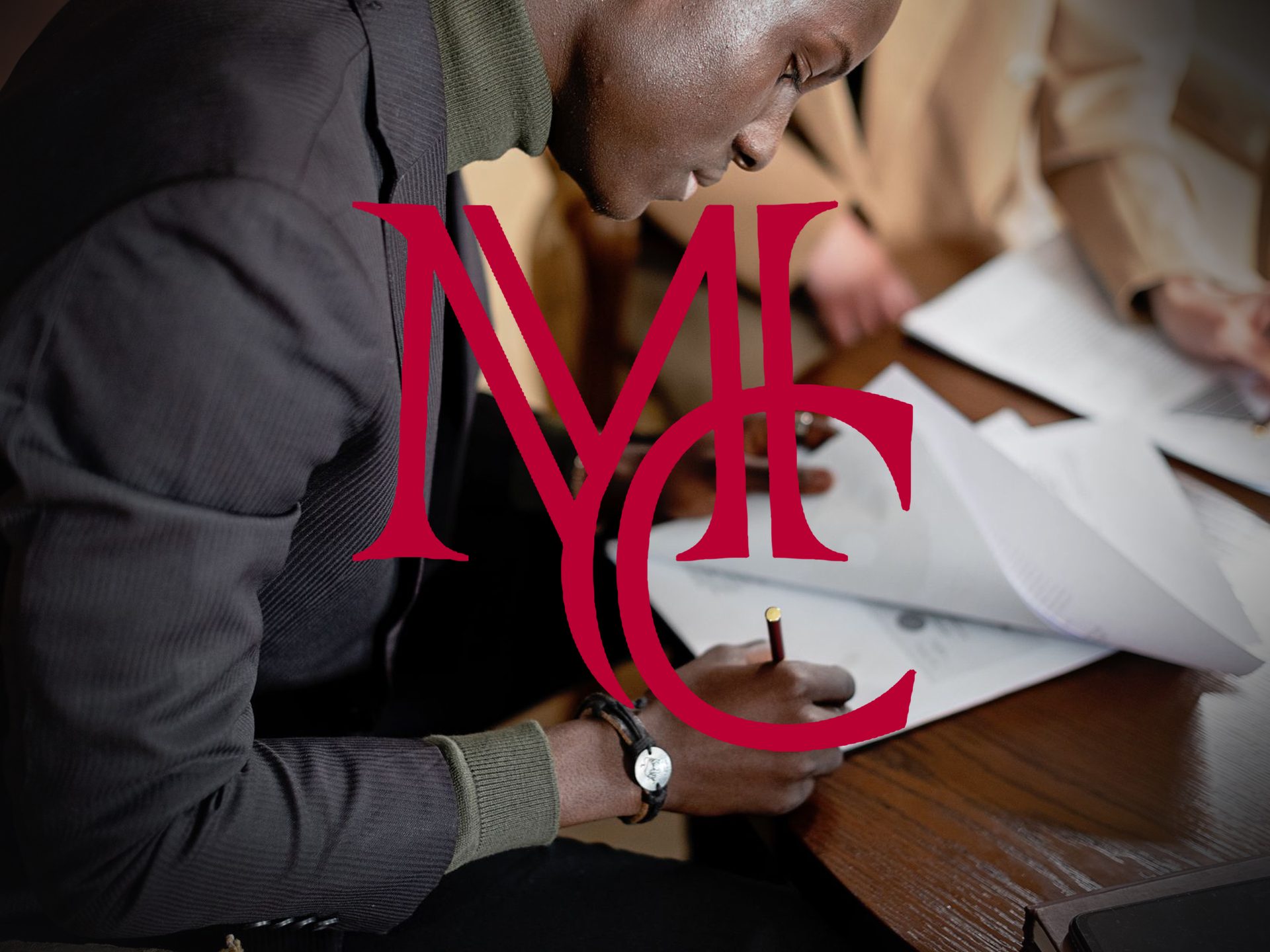 Man signing paperwork at a wooden table with the crimson Mason Capital Group monogram, illustrating selling a house with an assumable mortgage
