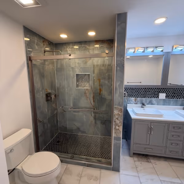 Bathroom remodel in Naperville IL – walk-in shower with large format marble tiles, sliding glass door, hexagon mosaic floor, gray vanity with vessel sink