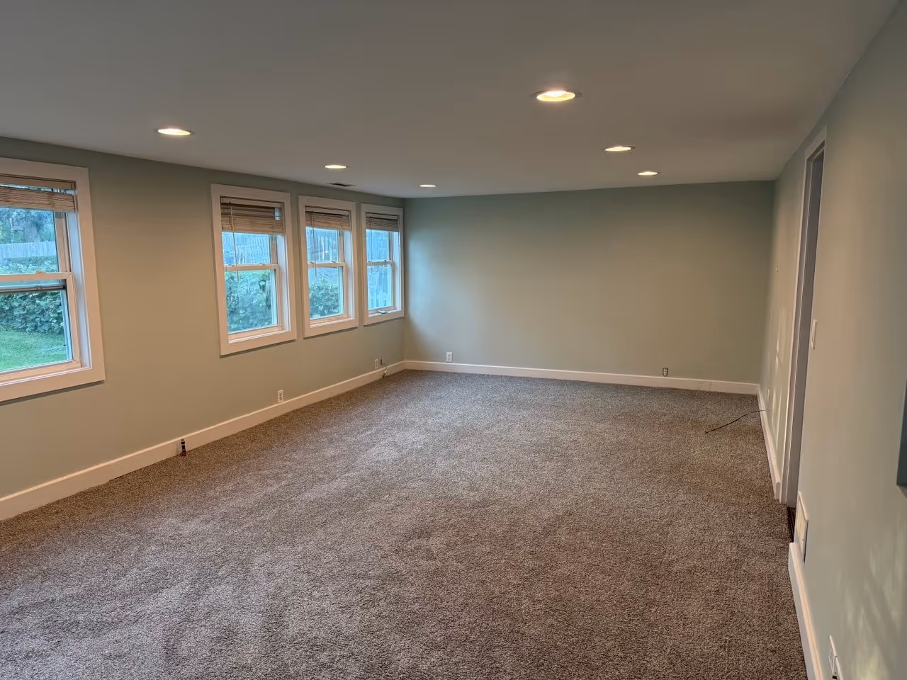 Sunroom remodel in Downers Grove IL – new carpet, painted walls, repaired drywall, and white baseboards with recessed lighting and large windows