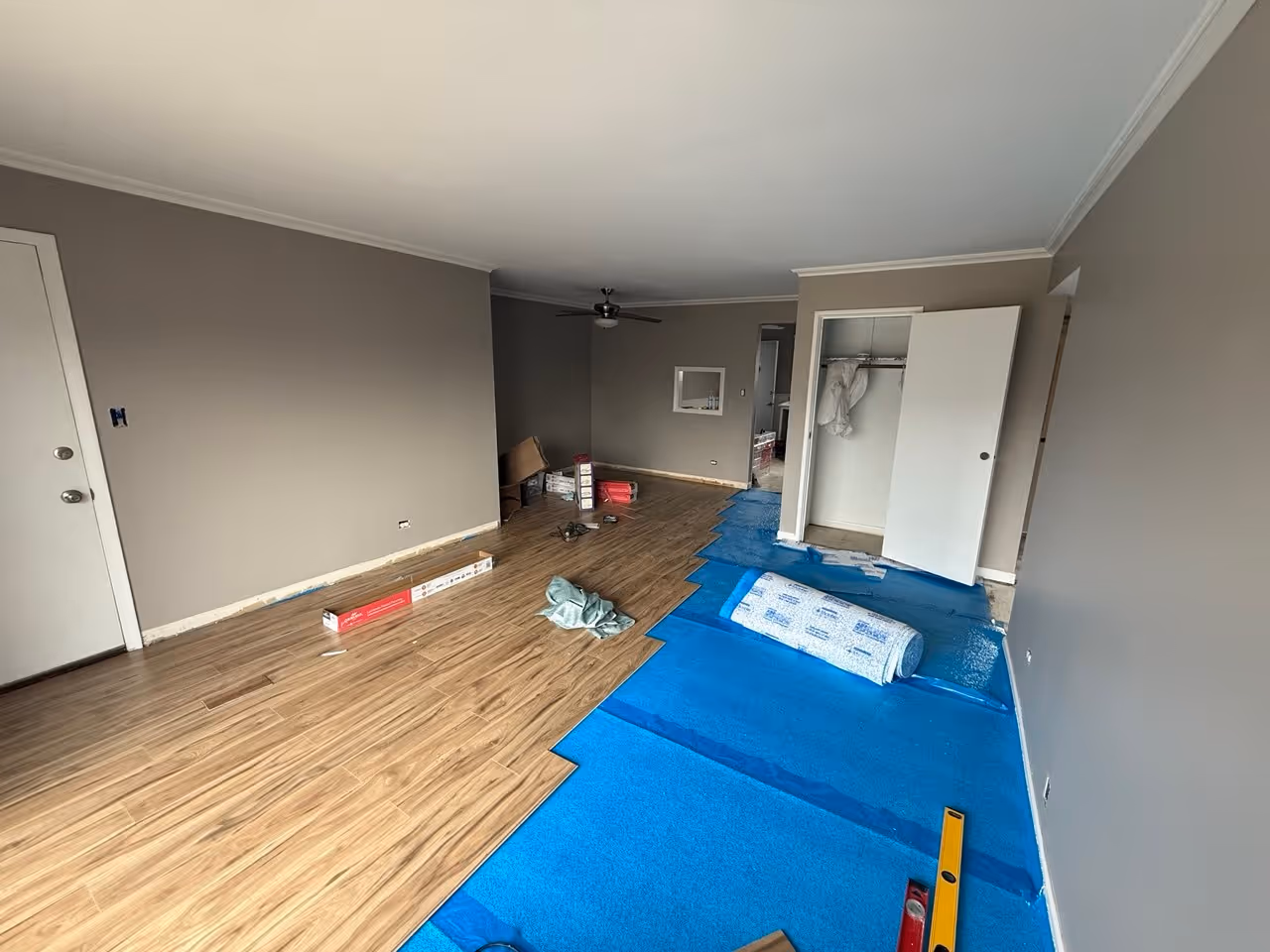 Flooring installation in progress with new plank flooring, blue underlayment, and partially finished residential room
