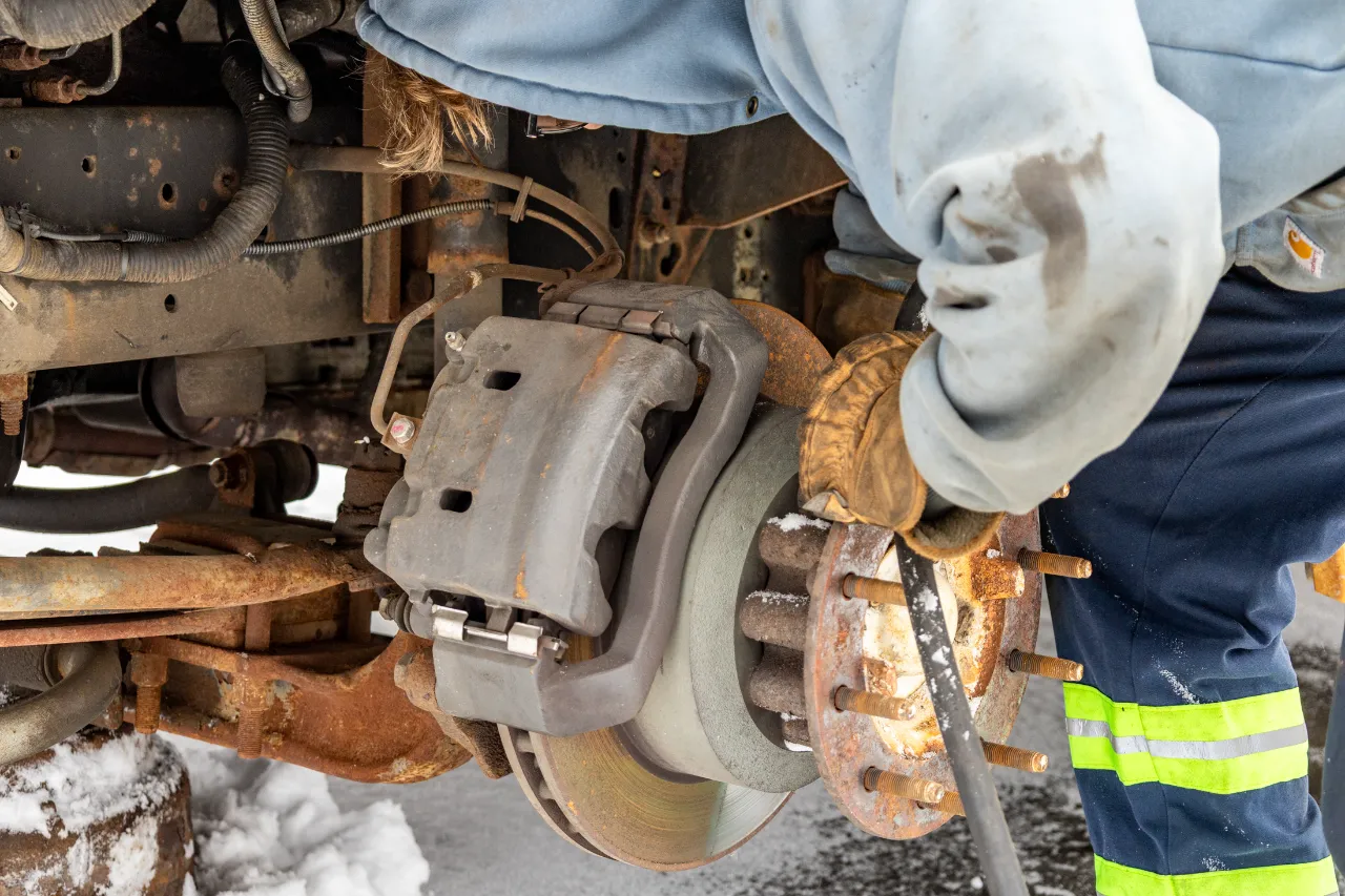 Brake repair on a heavy-duty truck as a technician services the exposed rotor and caliper assembly.