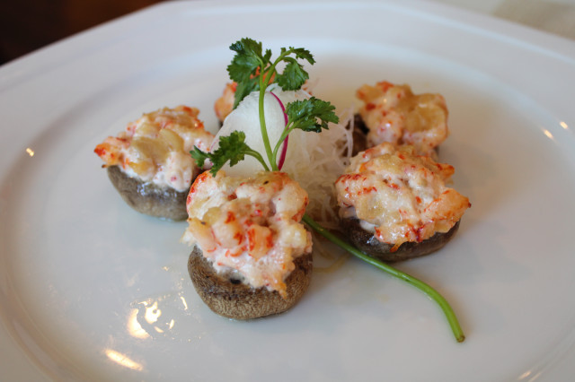 Five stuffed mushrooms topped with creamy seafood mixture and garnished with shredded daikon and a sprig of cilantro on a white plate.