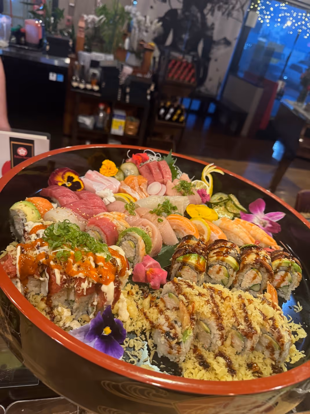 Large platter with assorted sushi rolls and sashimi garnished with edible flowers and greens.