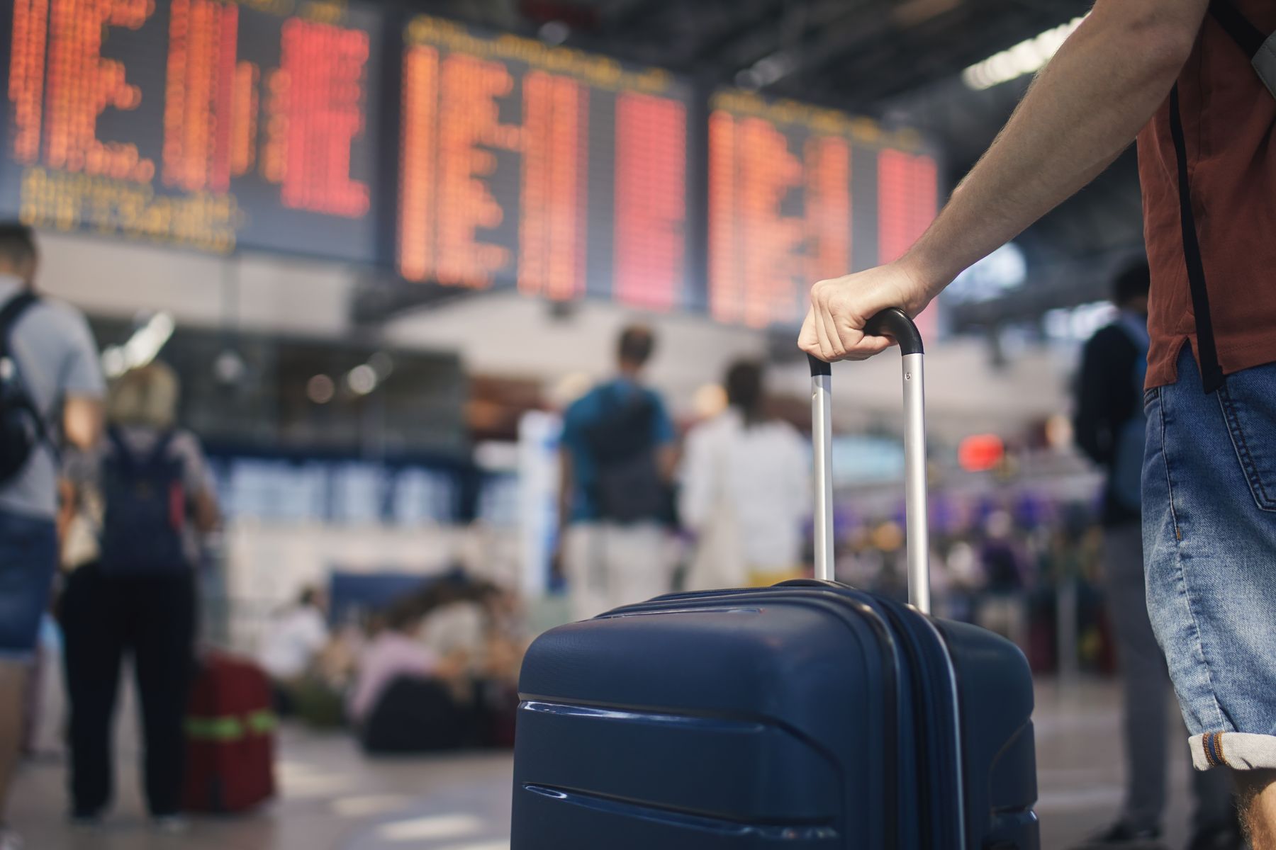 Traveller holding a suitcase in front of the departures board at an airport