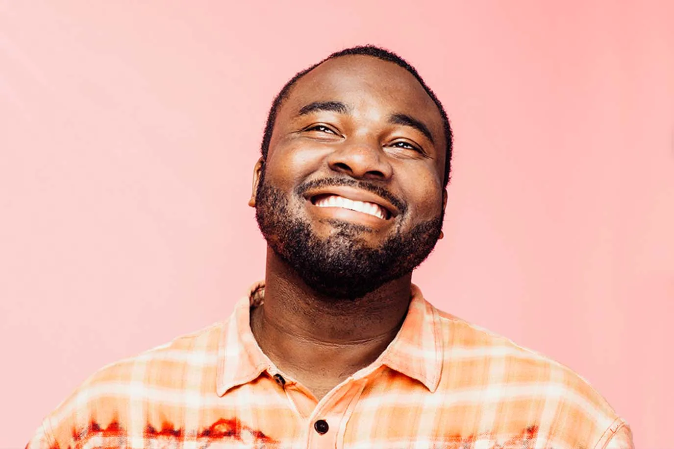 A man with a beard smiling and wearing a plaid shirt.
