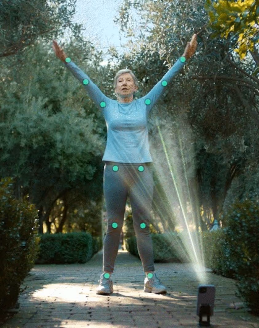 Woman outdoors performing stretching exercise with arms raised while recorded by a smartphone on a tripod.