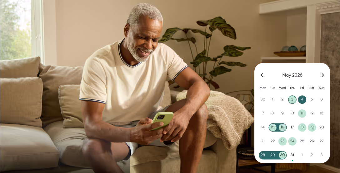 Smiling elderly man sitting on a couch looking at his phone with a May 2026 calendar overlay showing multiple highlighted dates.