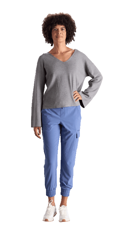 Person standing with one hand on hip, wearing gray long-sleeve top, blue pants, and white sneakers.
