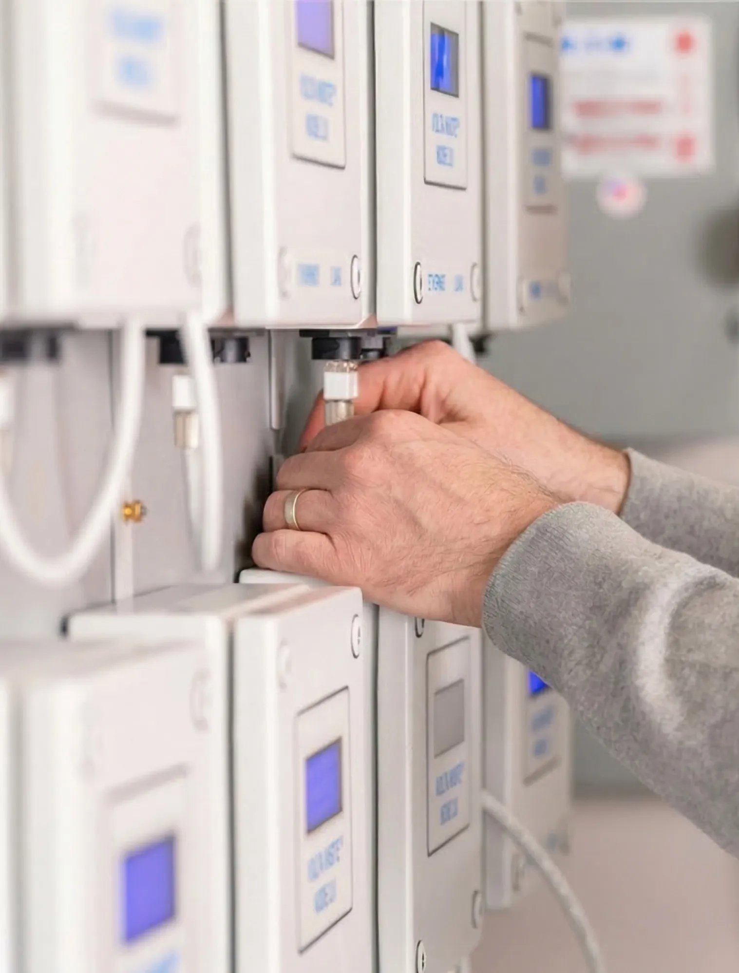 Hands adjusting a valve or knob on a row of white control panels with blue digital displays.