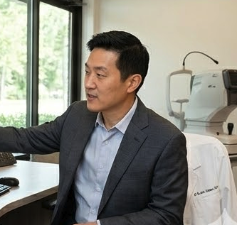Man in a suit sitting at a desk in an office with medical equipment in the background.