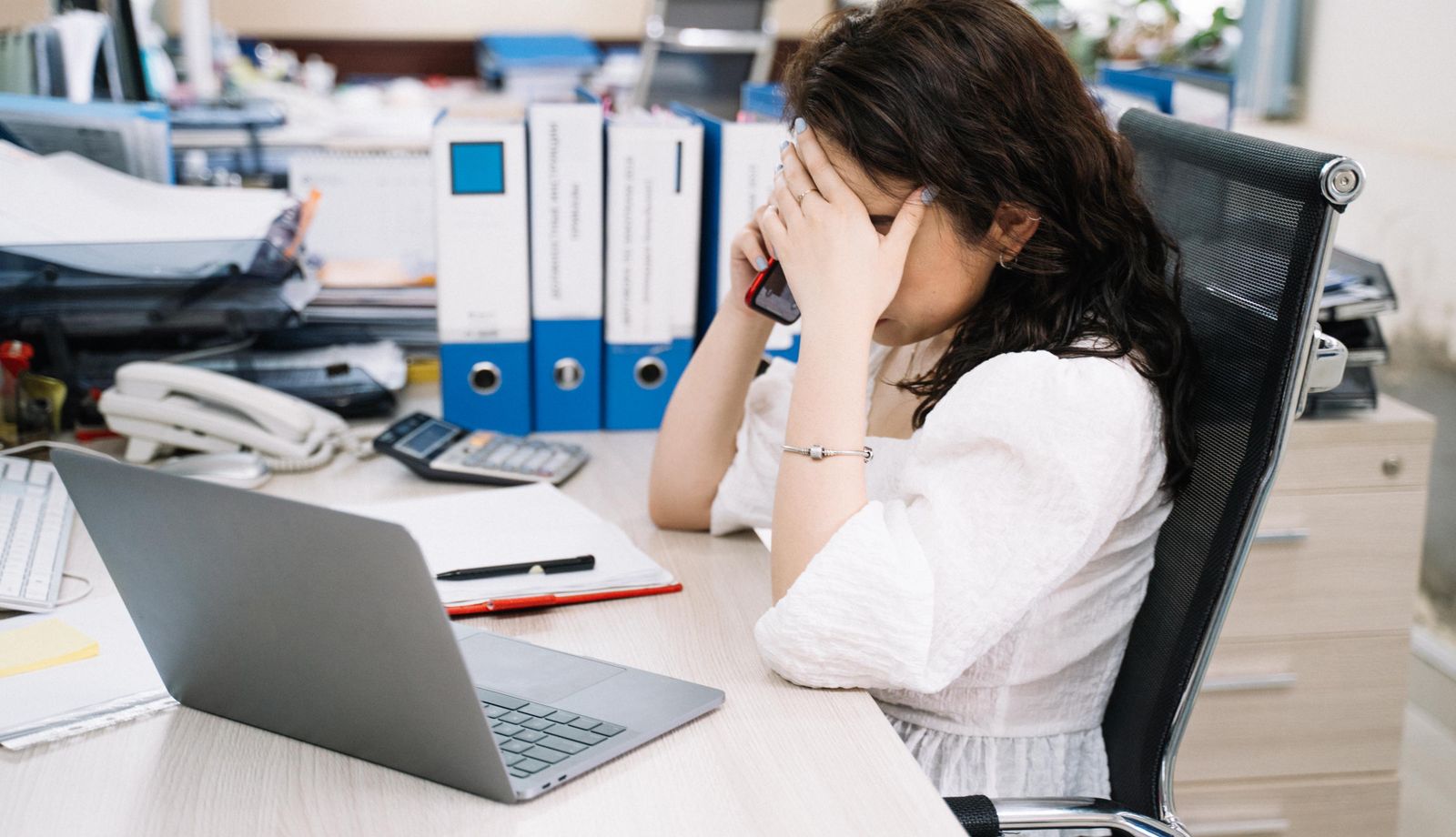 Overloaded front desk employee on the phone at a busy office desk