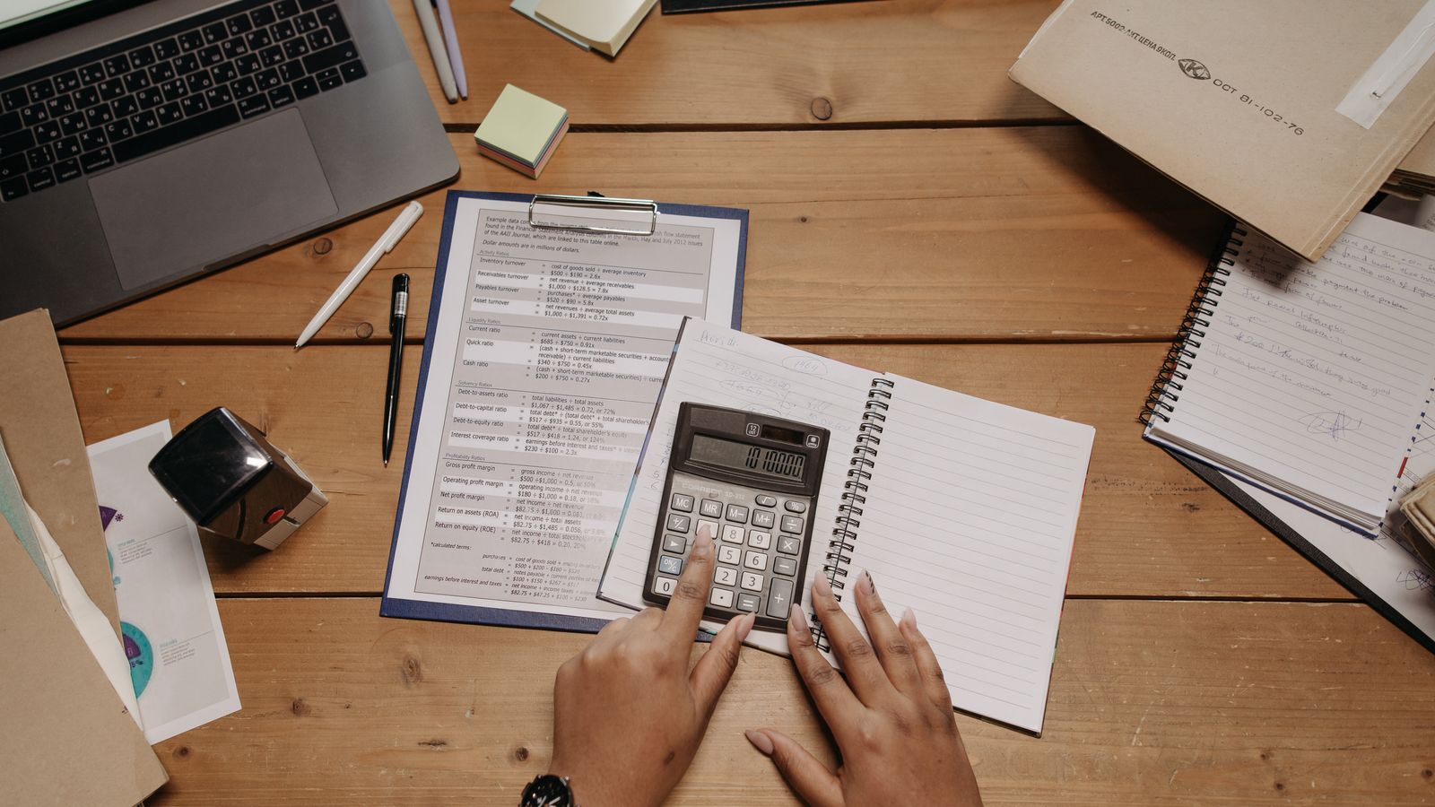 Hands working through practice cost calculations with a calculator and documents