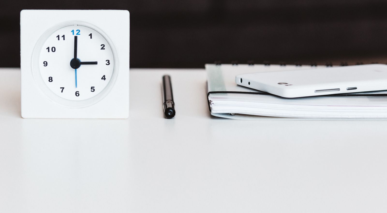 Desk with clock, notebook, and phone arranged for time management