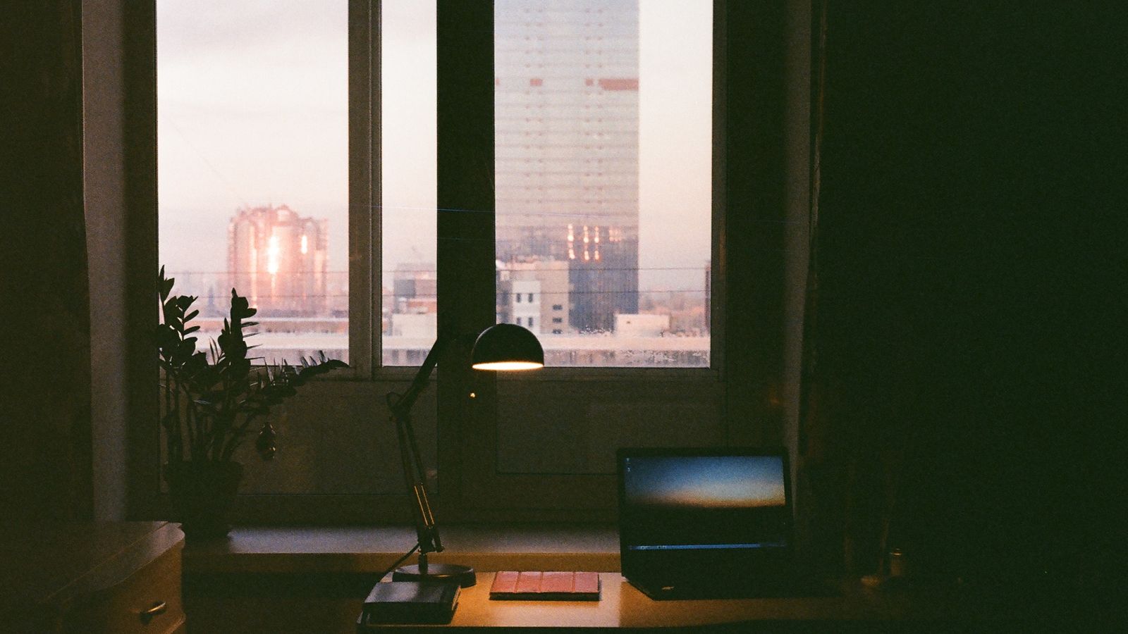 Desk with laptop and lamp overlooking a city at dusk