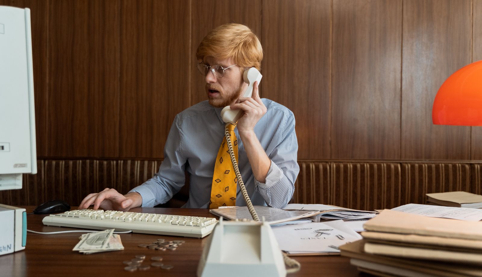 Man wearing eyeglasses taking a call on a landline phone at an office desk
