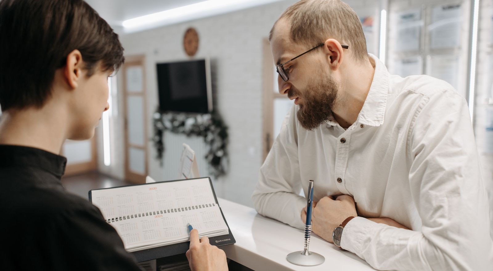 Receptionist reviewing an appointment book with a patient at a clinic counter