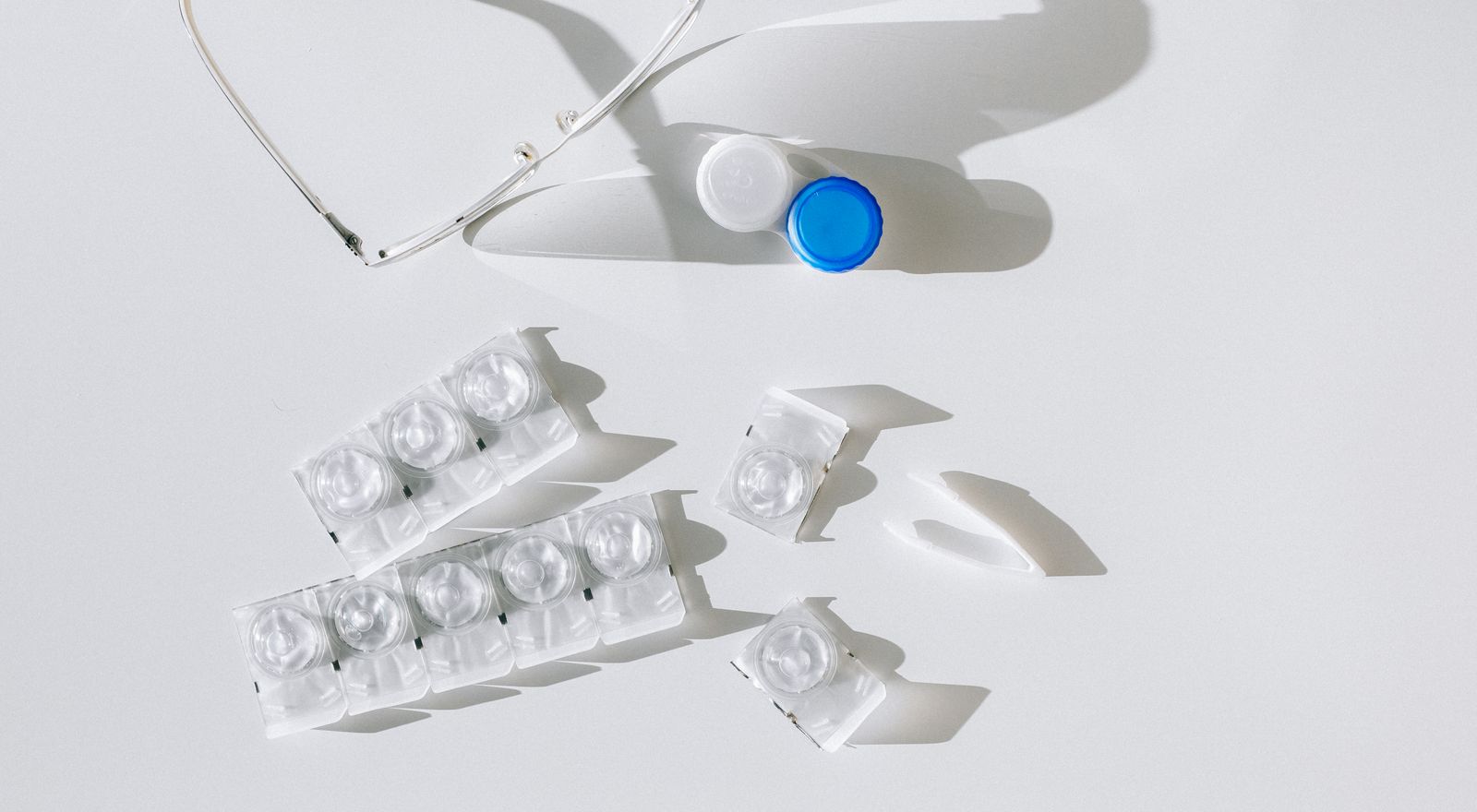 Contact lens packages, case, and eyeglasses arranged on a white surface