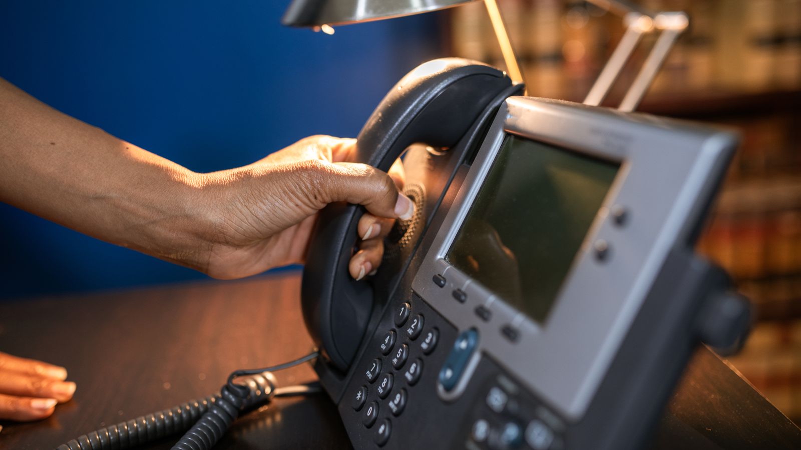 Hand lifting the handset of an office telephone at a front desk