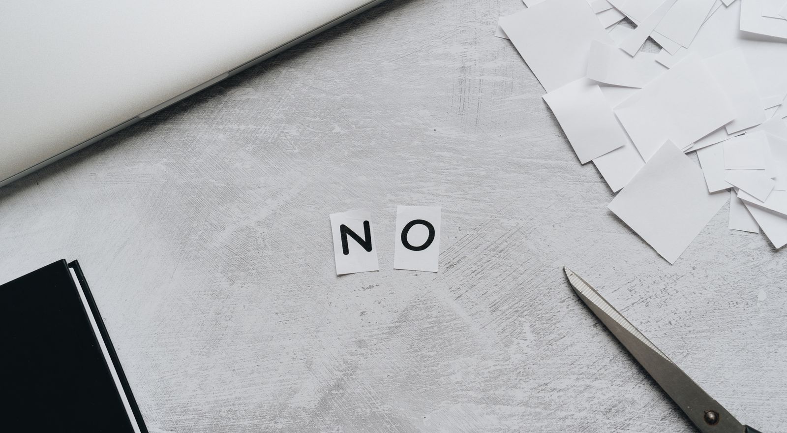 Scattered paper squares spelling the word no beside a laptop