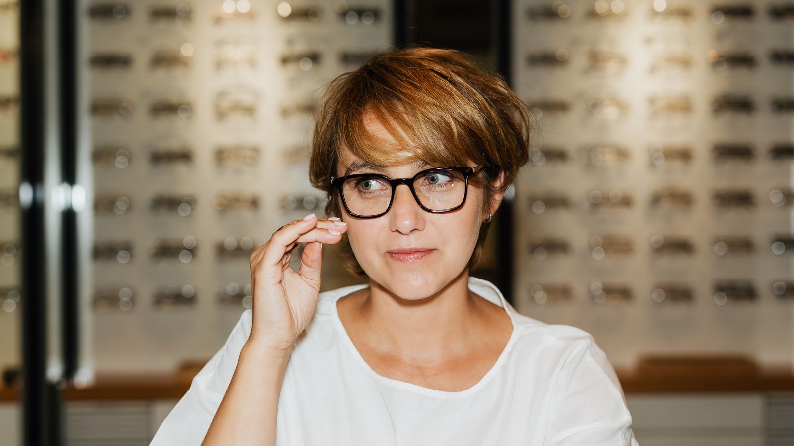 Customer checking new eyeglasses in front of an optical display wall