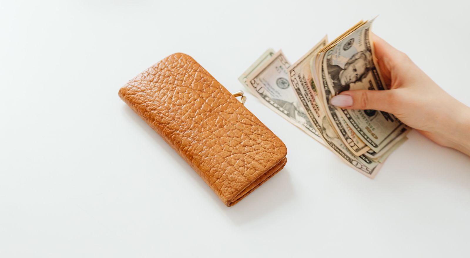 Hand counting dollar bills beside a leather wallet