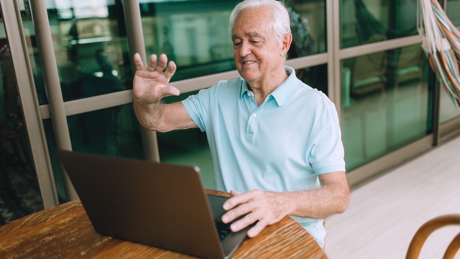 Senior patient waving during a video check-in on a laptop