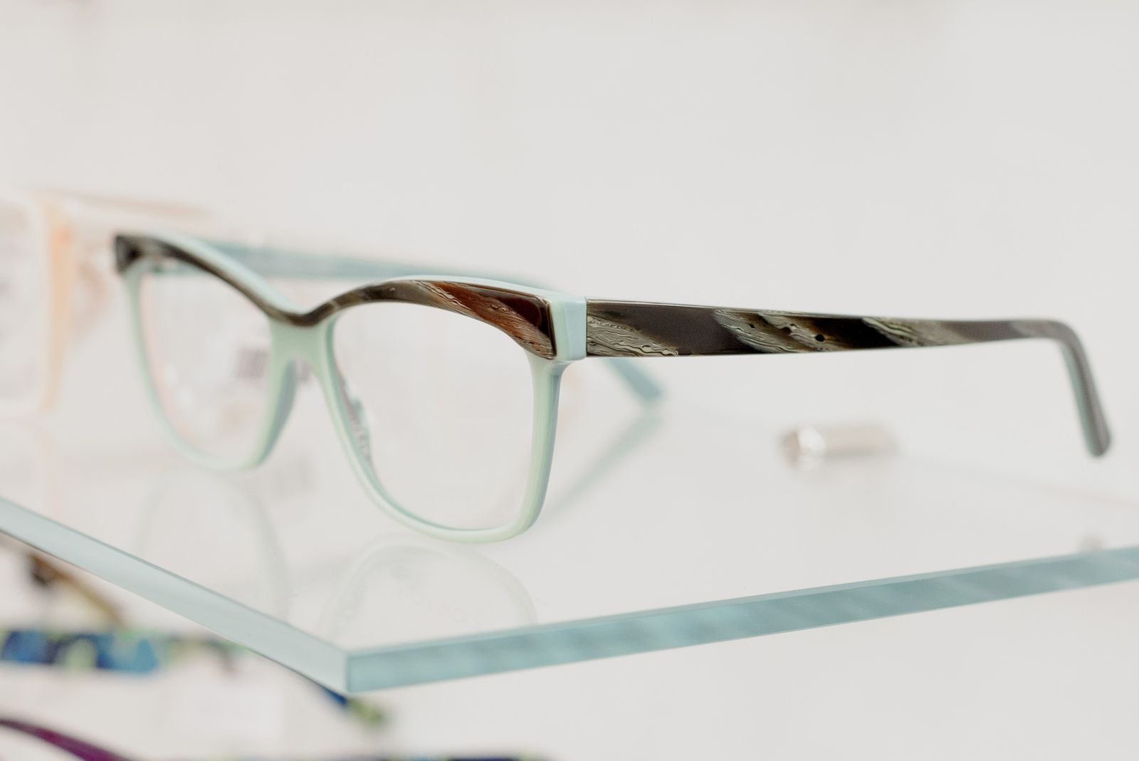 Modern eyeglasses displayed on a transparent shelf in an optical store