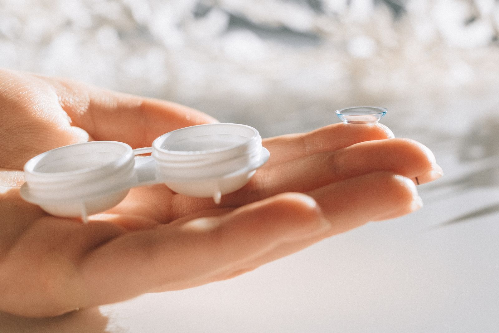 Hand holding a contact lens with a lens case nearby