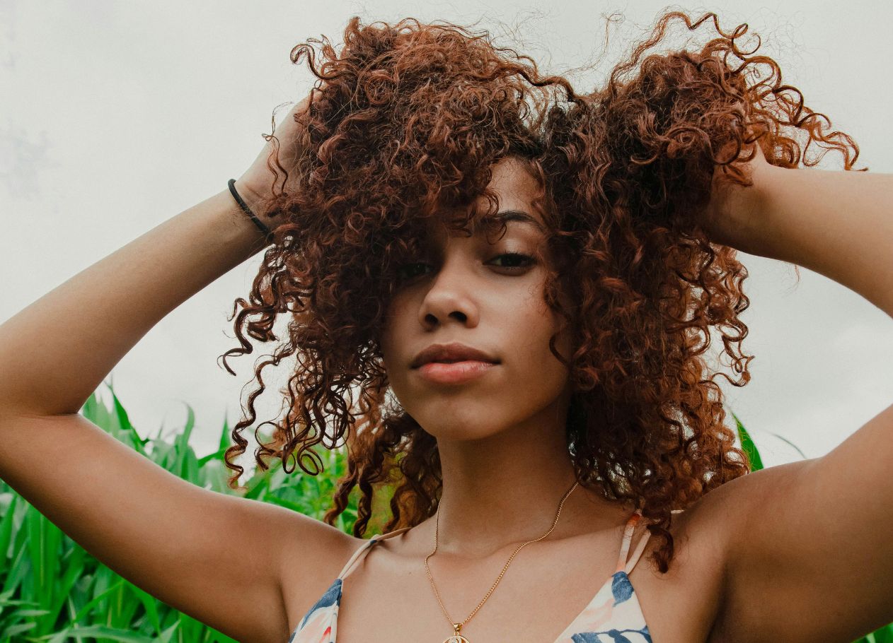 woman standing outside with hands in hair and tall plants behind her
