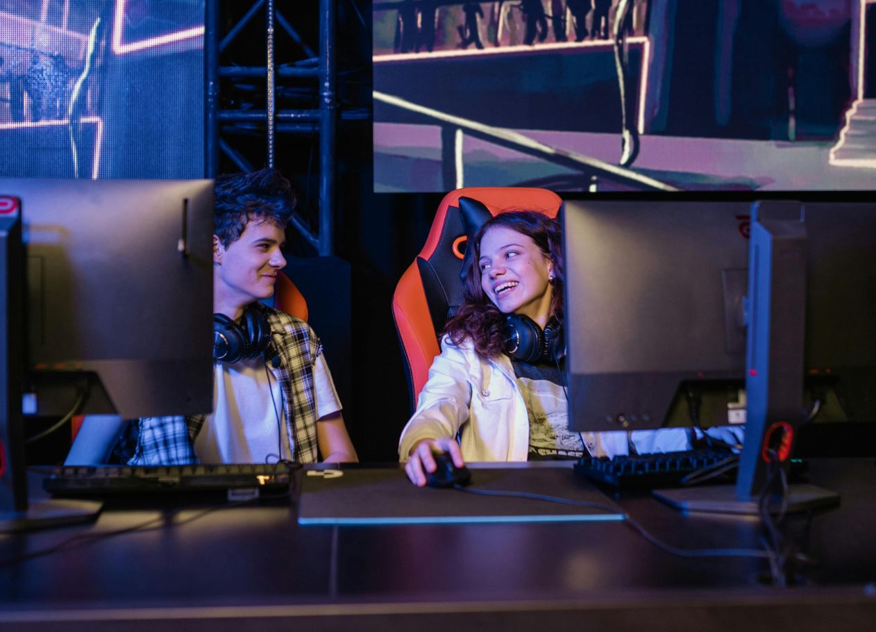 young man and woman laughing with each other sitting in front of computers in dark room used for gaming 