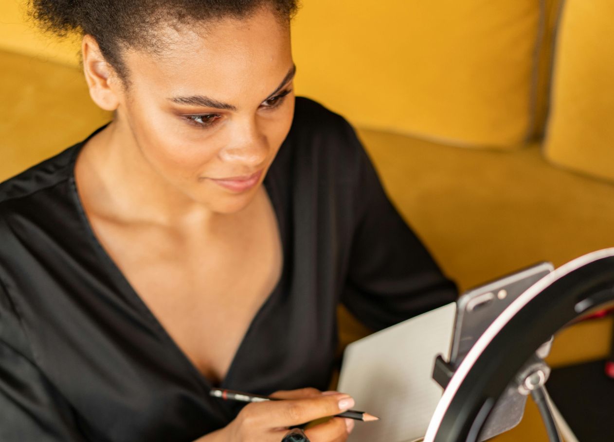 woman looking at cell phone with ring light around while she records with yellow sofa behind her